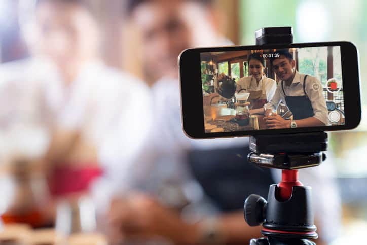 A photo of a phone recording two chefs as they make a meal together for digital marketing.