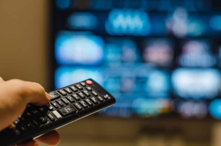 A person holding a TV remote with the TV screen blurred out in the background.