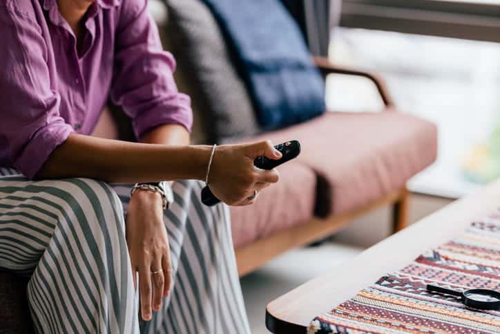 A woman holding a TV remote in her hand as she sits on the couch.