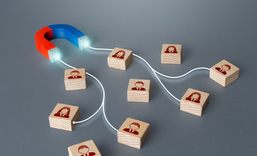 A red and blue horseshoe magnet attracting wooden blocks with red silhouette icons of people, connected by white lines, symbolizing traffic conversion.