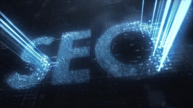 A holographic digital display featuring the text "SEO" in large blue letters with particle effects and glowing light beams on a dark grid background.