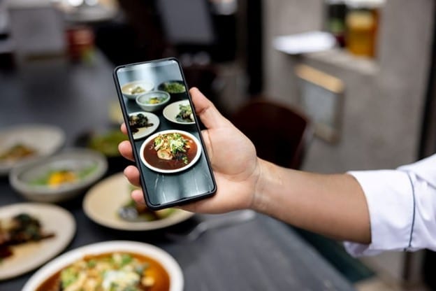 Smartphone displaying plated restaurant dishes, representing mobile-first restaurant digital marketing, online food promotion, and customer engagement.